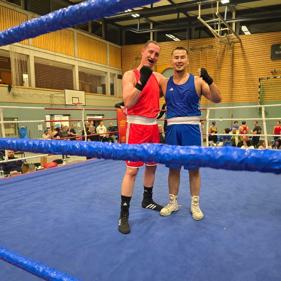Zwei Boxer in roten und blauen Shorts posieren erfreut nach einem Kampf im Ring.