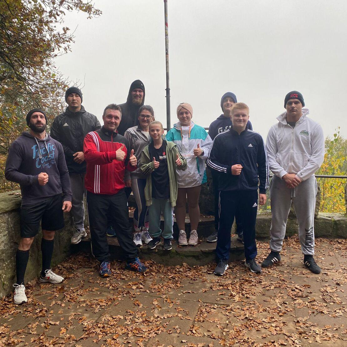 Gruppe von zehn Personen posiert auf einem Weg im Wald, umgeben von herbstlichen Blättern und Nebel.