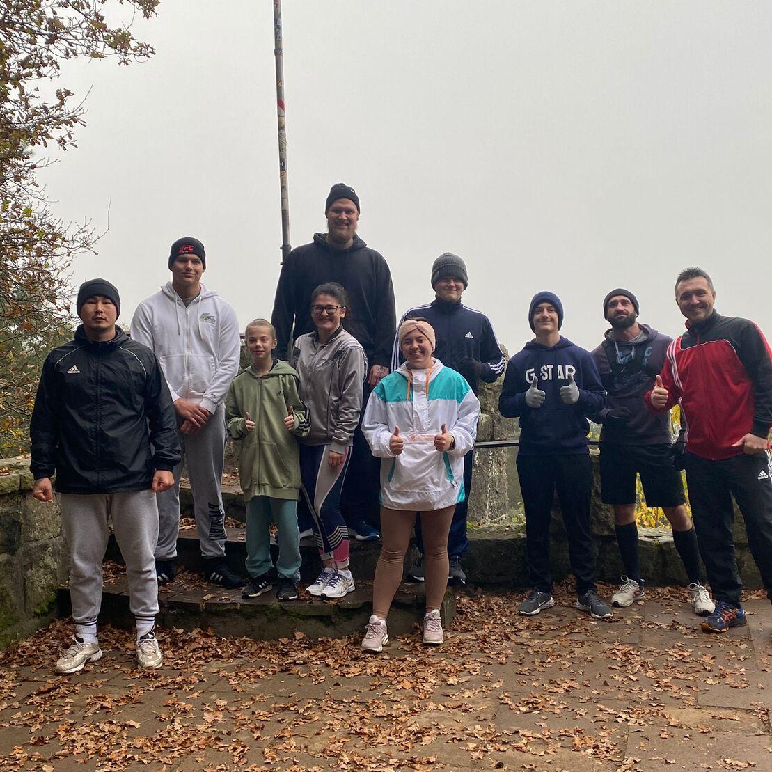 Gruppe von acht Personen in Sportkleidung posiert auf einem Aussichtspunkt umgeben von herbstlichen Blättern.