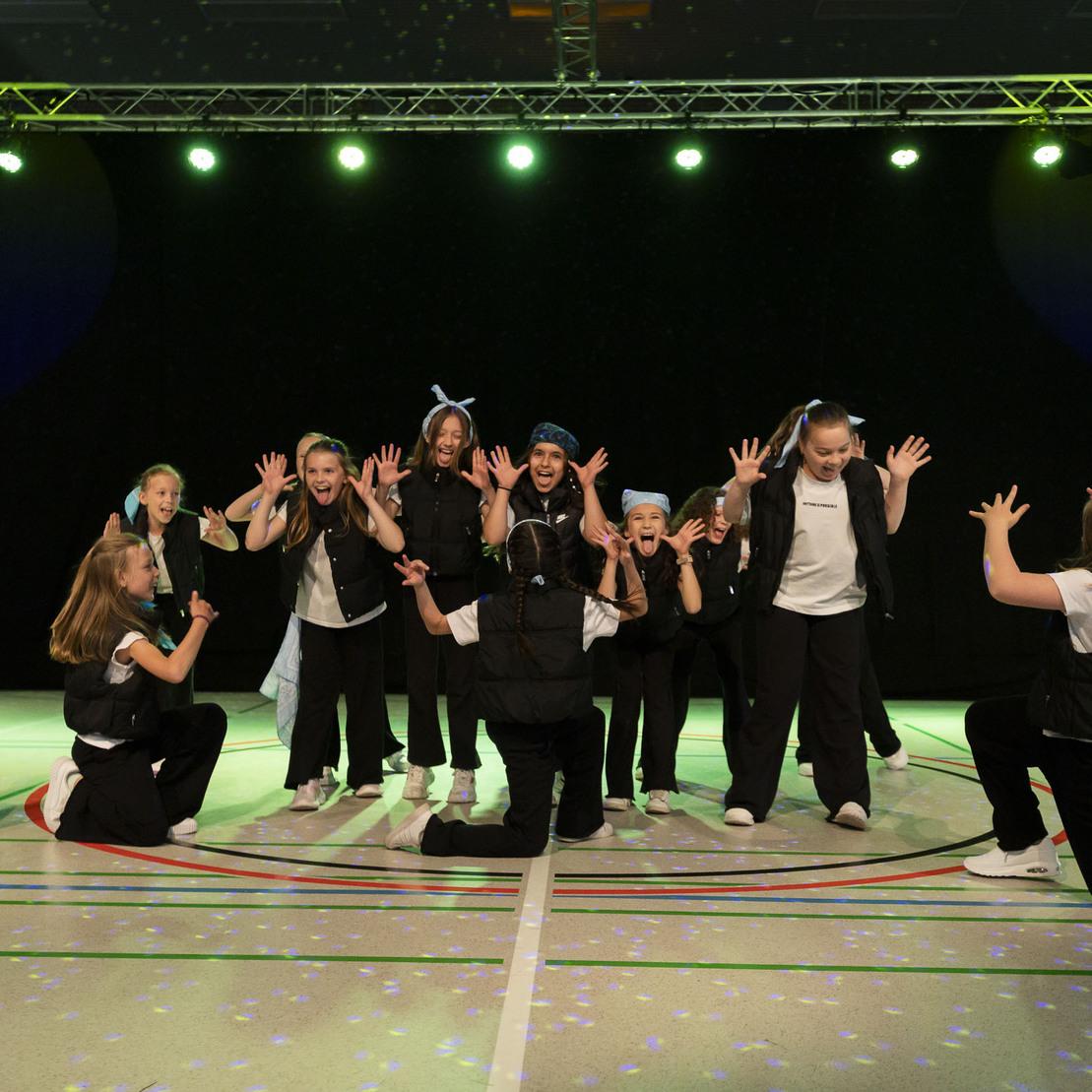 Gruppe von Kindern in Tanzuniformen pr&auml;sentiert eine choreografierte Auff&uuml;hrung auf einer B&uuml;hne mit farbigen Lichtern.
