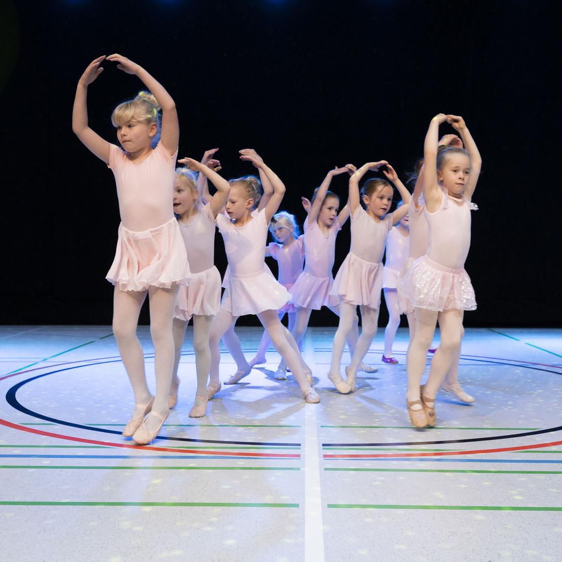Gruppe junger Ballettt&auml;nzerinnen in rosa Kost&uuml;men tanzt auf einer beleuchteten B&uuml;hne mit farbigen Linien.
