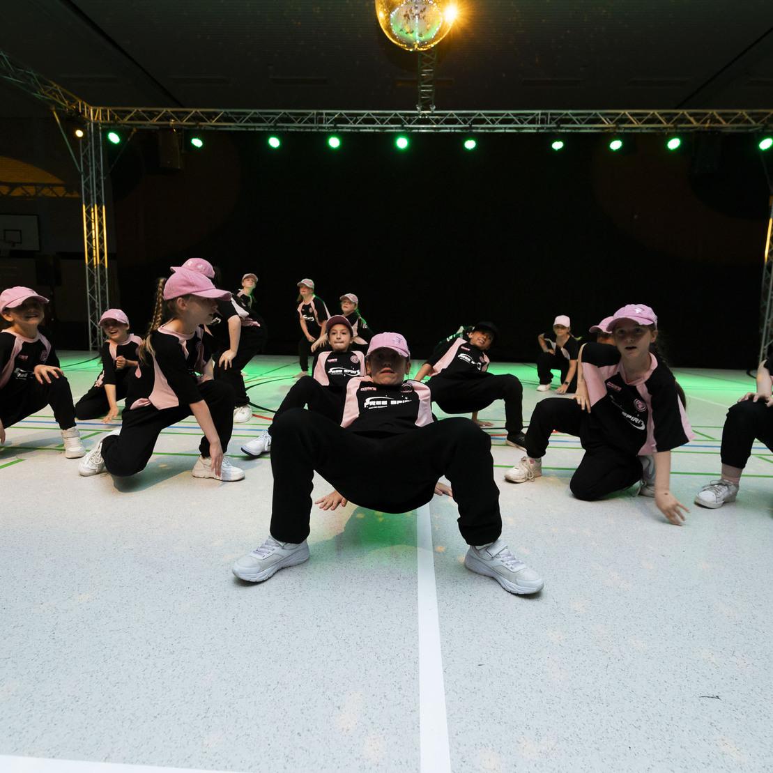 Tanzgruppe in Schwarz und Pink f&uuml;hrt eine choreografierte Darbietung mit geteilten Bewegungen auf einer Sportfl&auml;che vor.