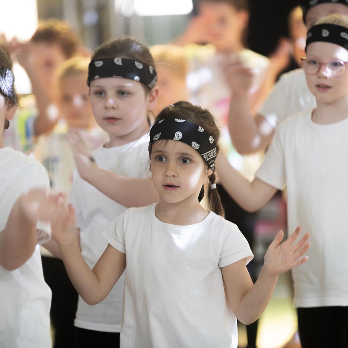 Gruppe von Kindern in wei&szlig;en T-Shirts und schwarzen Bandanas bei einer Tanzauff&uuml;hrung.
