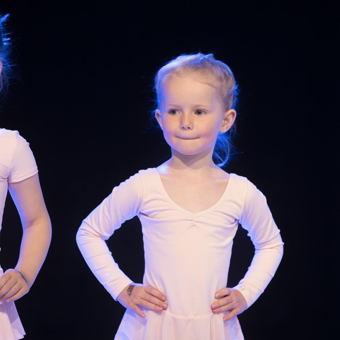 Zwei kleine Ballettt&auml;nzerinnen in rosa Leibchen stehen auf einer B&uuml;hne mit dunklem Hintergrund.