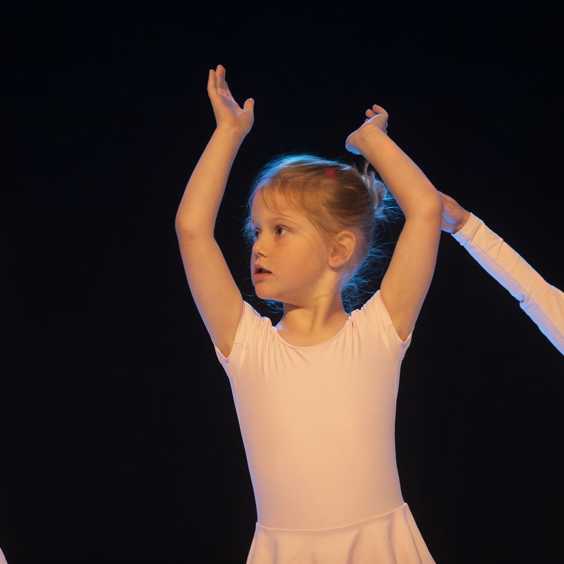 Drei kleine Ballettt&auml;nzerinnen in wei&szlig;en Kost&uuml;men, die auf einer B&uuml;hne mit blauem Licht posieren.