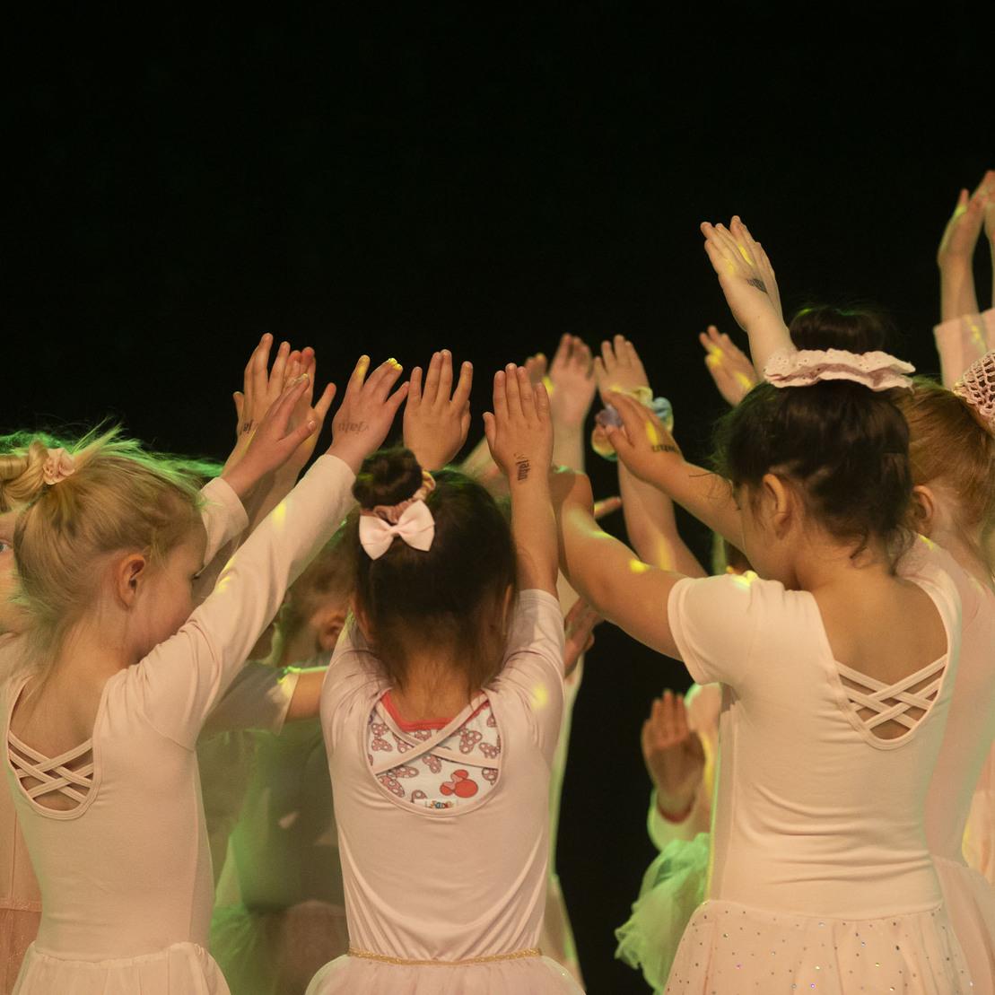 Gruppe von Ballettt&auml;nzerinnen in wei&szlig;en Kost&uuml;men, die mit erhobenen H&auml;nden eine Choreografie ausf&uuml;hren.