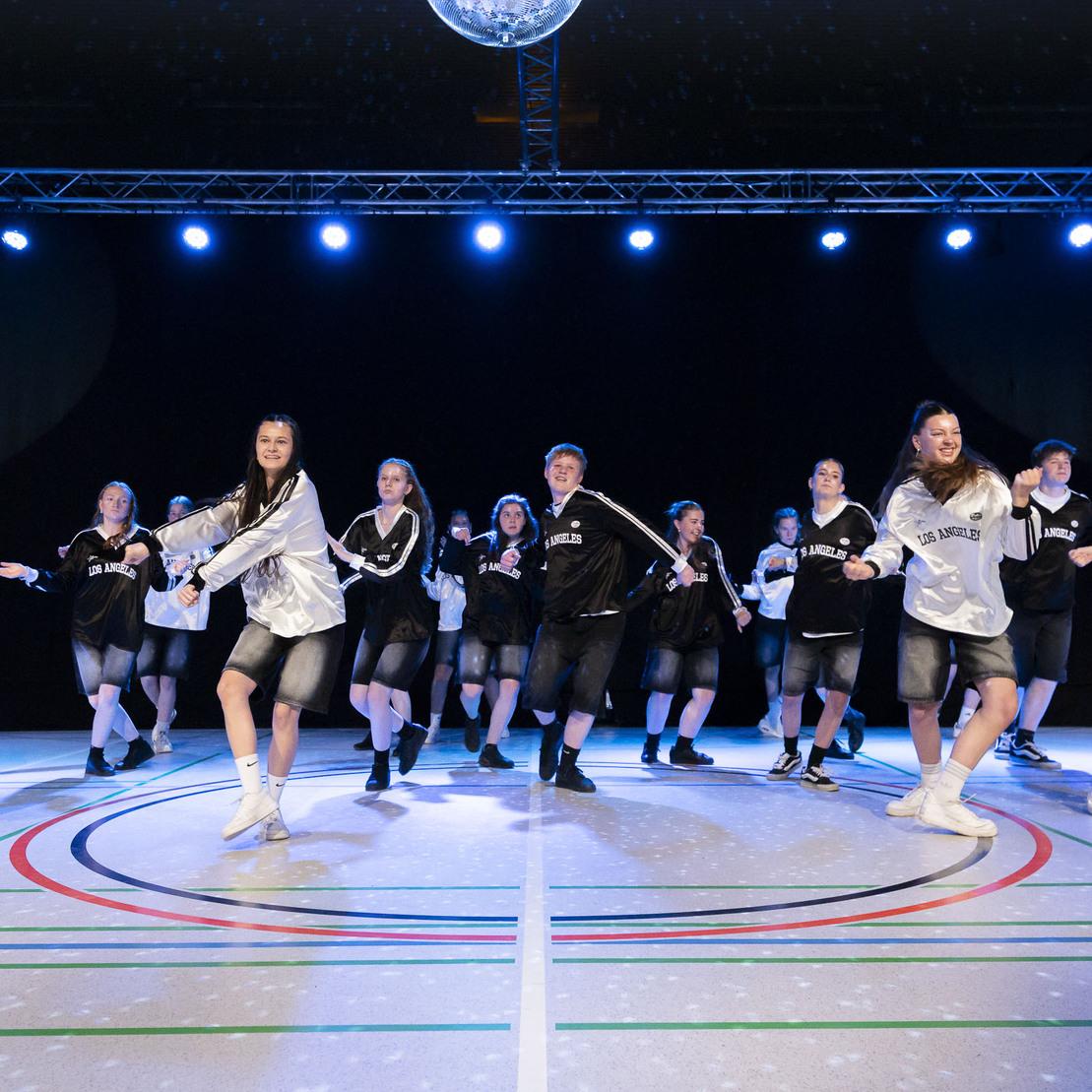 Tanzgruppe in sportlichen Outfits f&uuml;hrt eine synchronisierte Choreografie auf einer beleuchteten B&uuml;hne durch.