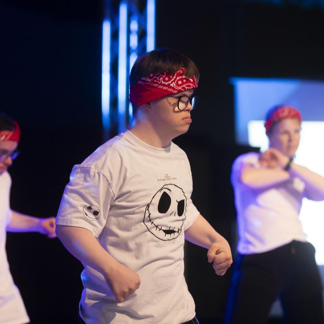 Drei T&auml;nzer in Bandanas f&uuml;hren eine choreografierte Performance auf einer B&uuml;hne mit blauer Beleuchtung vor.