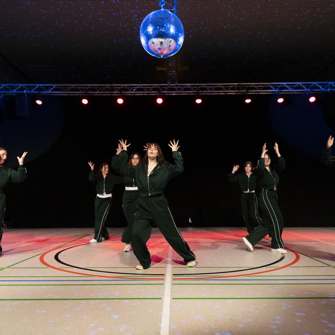 Tanzgruppe in gr&uuml;nen Trainingsanz&uuml;gen f&uuml;hrt eine Choreografie unter einem Discokugel-Licht auf.
