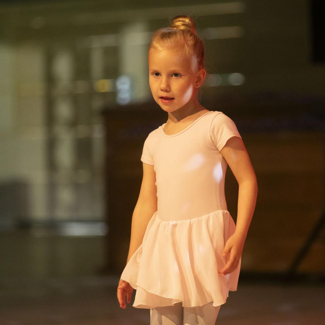 M&auml;dchen in einem rosa Ballettkleid steht auf einer B&uuml;hne mit unscharfem Hintergrund.