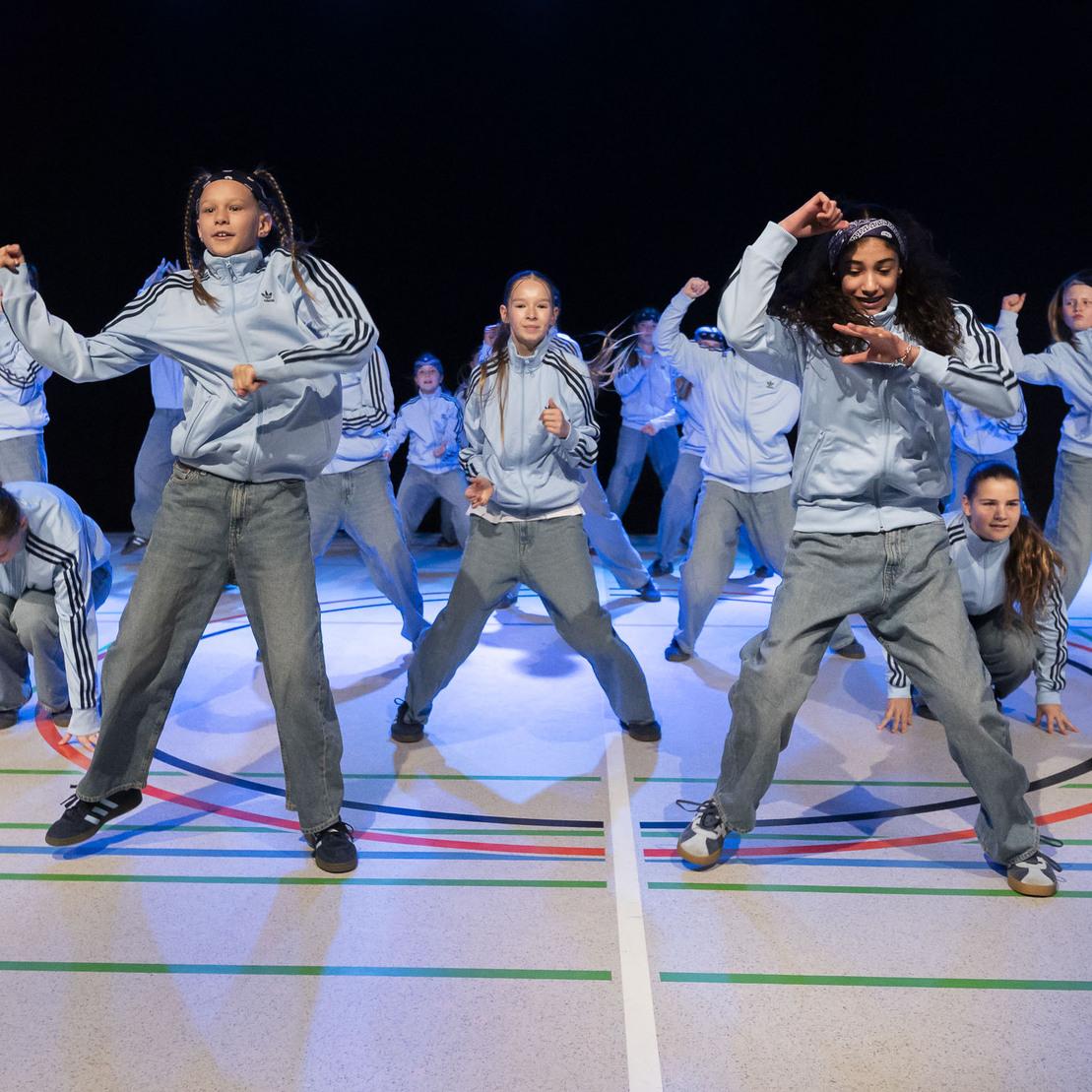 Tanzgruppe in Sportkleidung f&uuml;hrt Choreografie auf einer beleuchteten Sportfl&auml;che mit Linien und Kreisen auf.