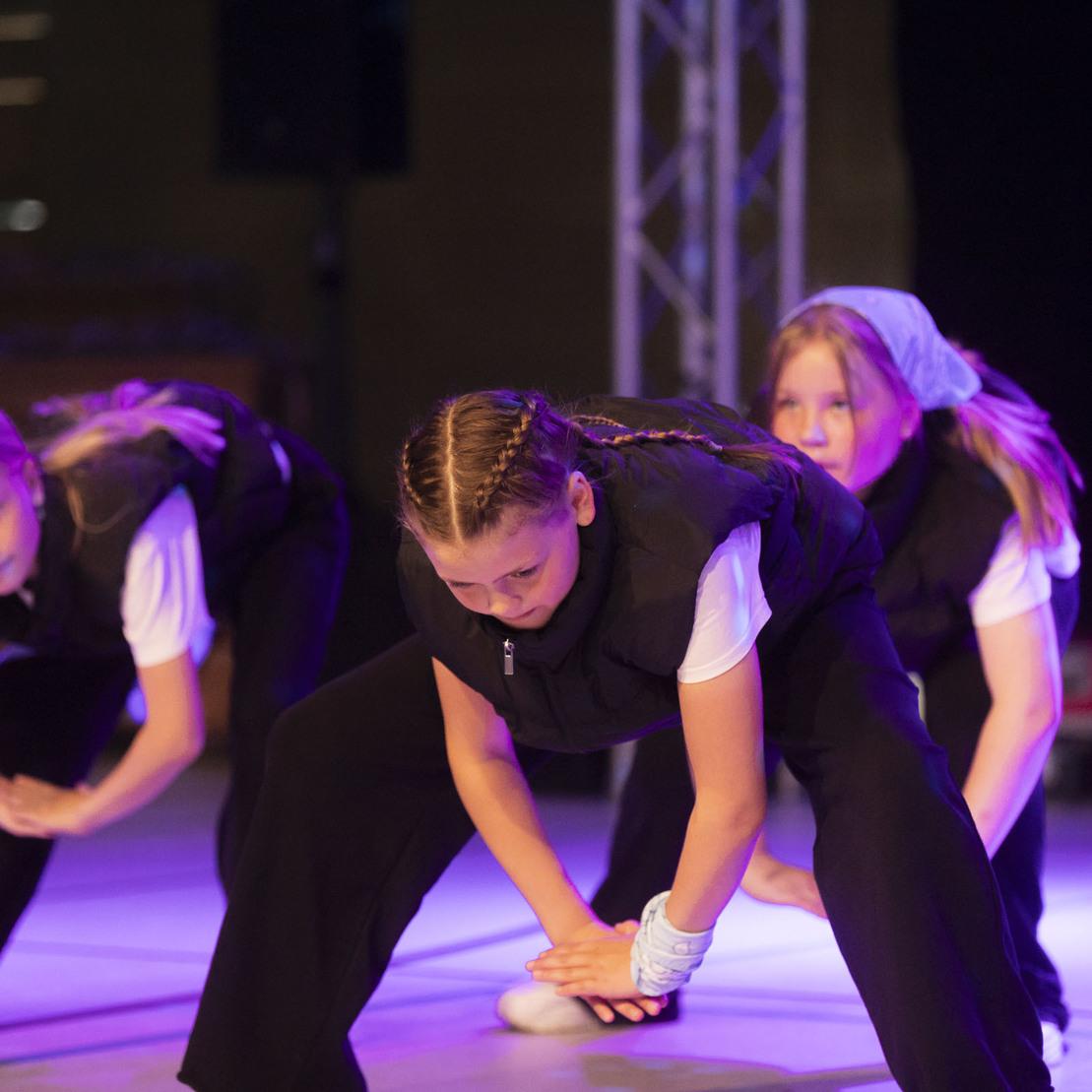 Drei T&auml;nzerinnen in schwarz-wei&szlig;er Kleidung f&uuml;hren eine choreografierte Bewegung auf einer B&uuml;hne aus.