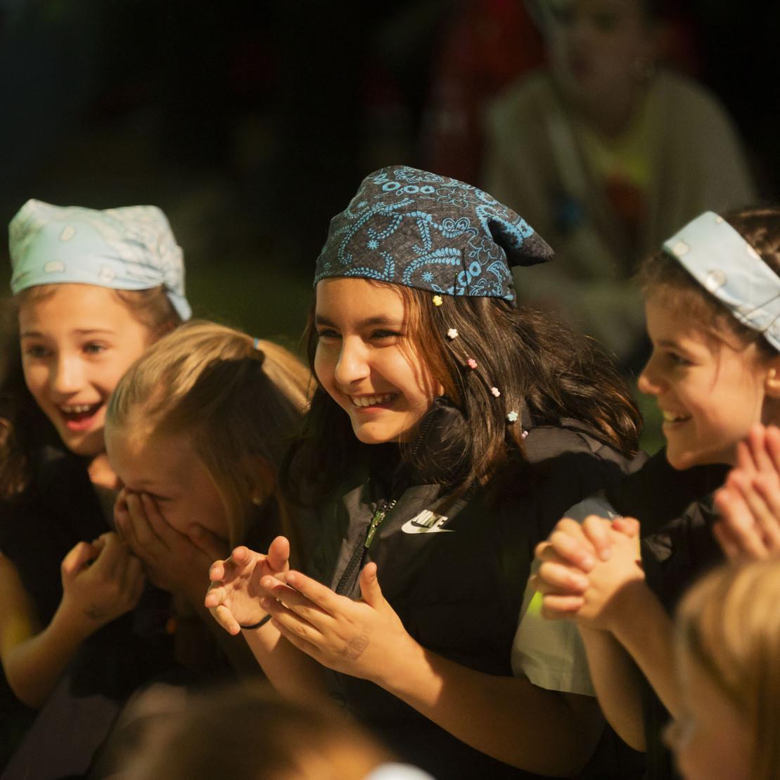 Gruppe von fr&ouml;hlichen M&auml;dchen mit Kopfband, die clapping und l&auml;cheln auf einem Event oder einer Auff&uuml;hrung.