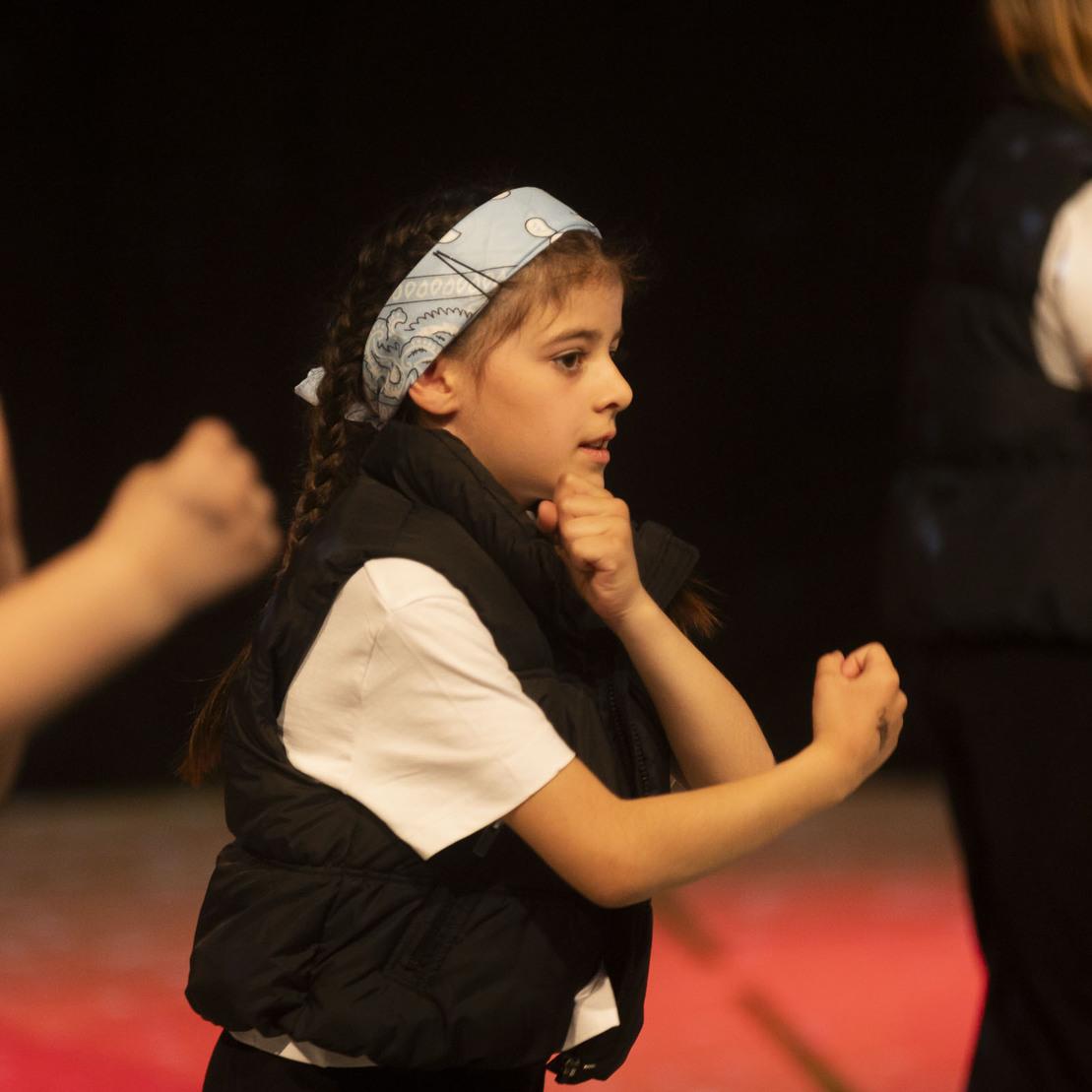 Tanzende Kinder in schwarz-wei&szlig;er Kleidung, eines mit blauer Kopfbinde, f&uuml;hren eine choreografierte Performance auf.