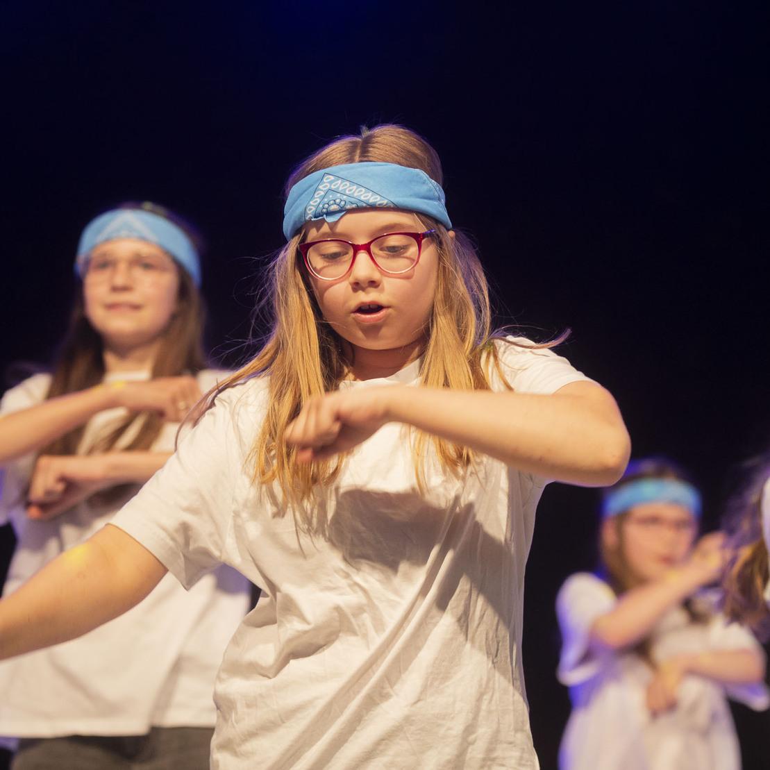 Tanzende Kinder in wei&szlig;en T-Shirts und blauen Stirnb&auml;ndern f&uuml;hren eine Choreografie auf.