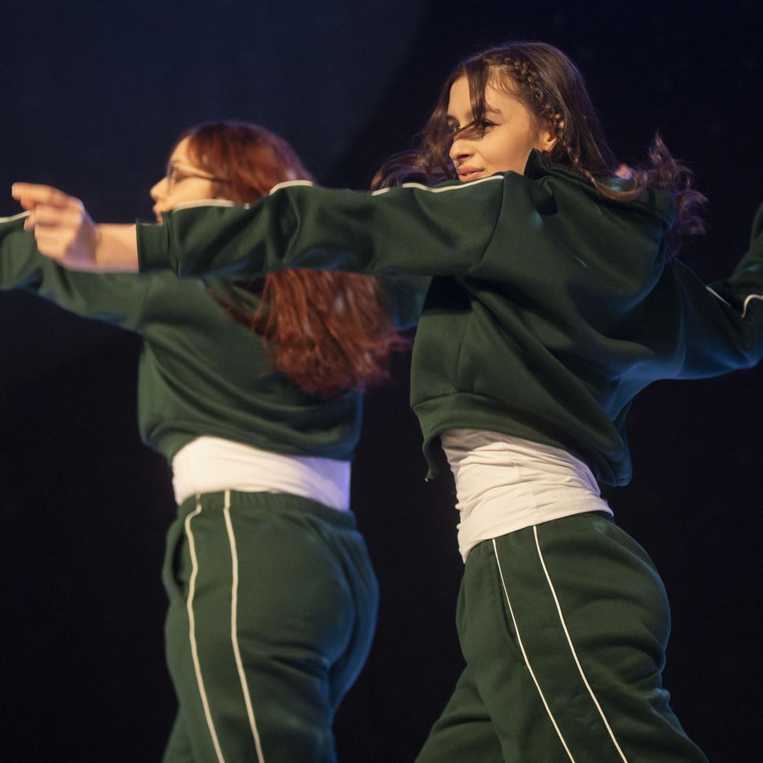 Zwei T&auml;nzerinnen in gr&uuml;nen Sportanz&uuml;gen f&uuml;hren synchron eine Choreografie auf einer B&uuml;hne aus.