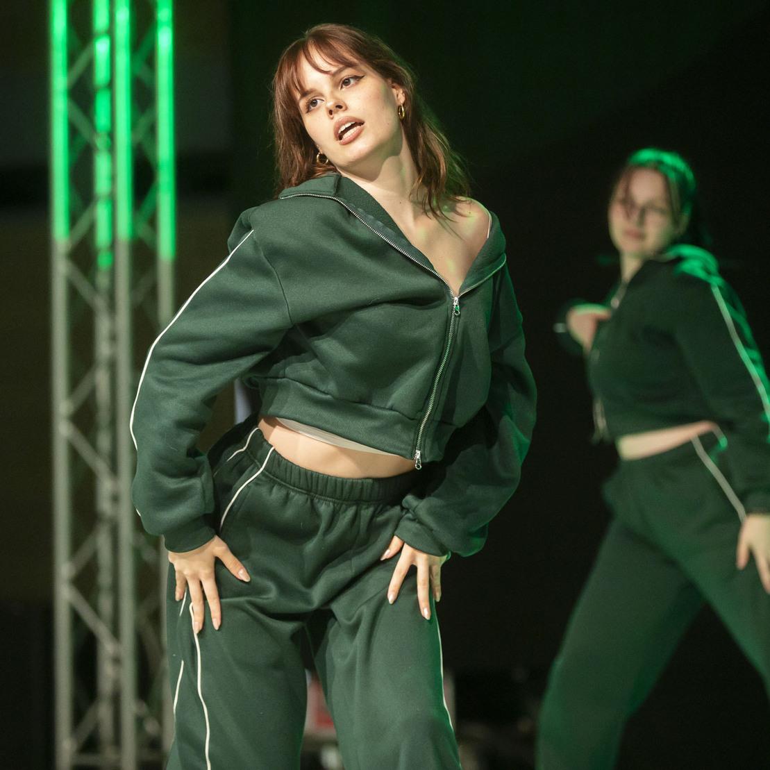 T&auml;nzerin in gr&uuml;ner Sportbekleidung pr&auml;sentiert eine ausdrucksstarke Tanzpose auf einer Veranstaltung.