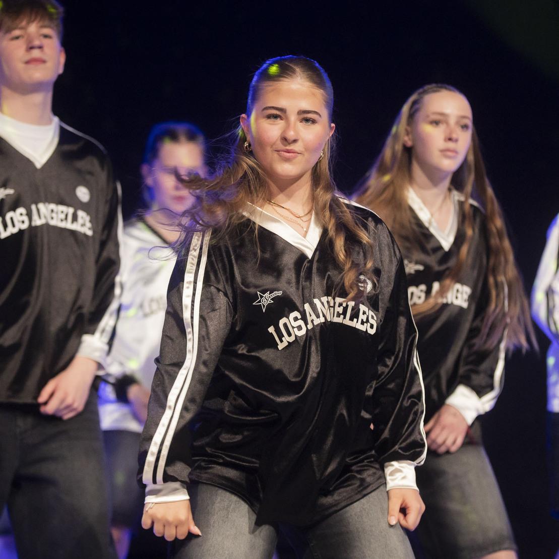 Tanzgruppe in schwarzen und wei&szlig;en Oberteilen f&uuml;hrt eine choreografierte Darbietung auf einer B&uuml;hne auf.