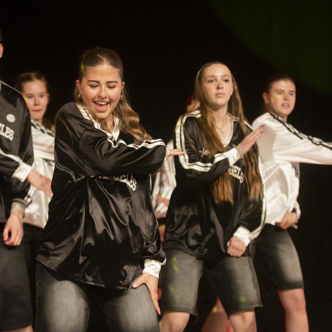 Tanzgruppe in sportlicher Kleidung f&uuml;hrt eine einstudierte Choreografie auf einer B&uuml;hne vor.