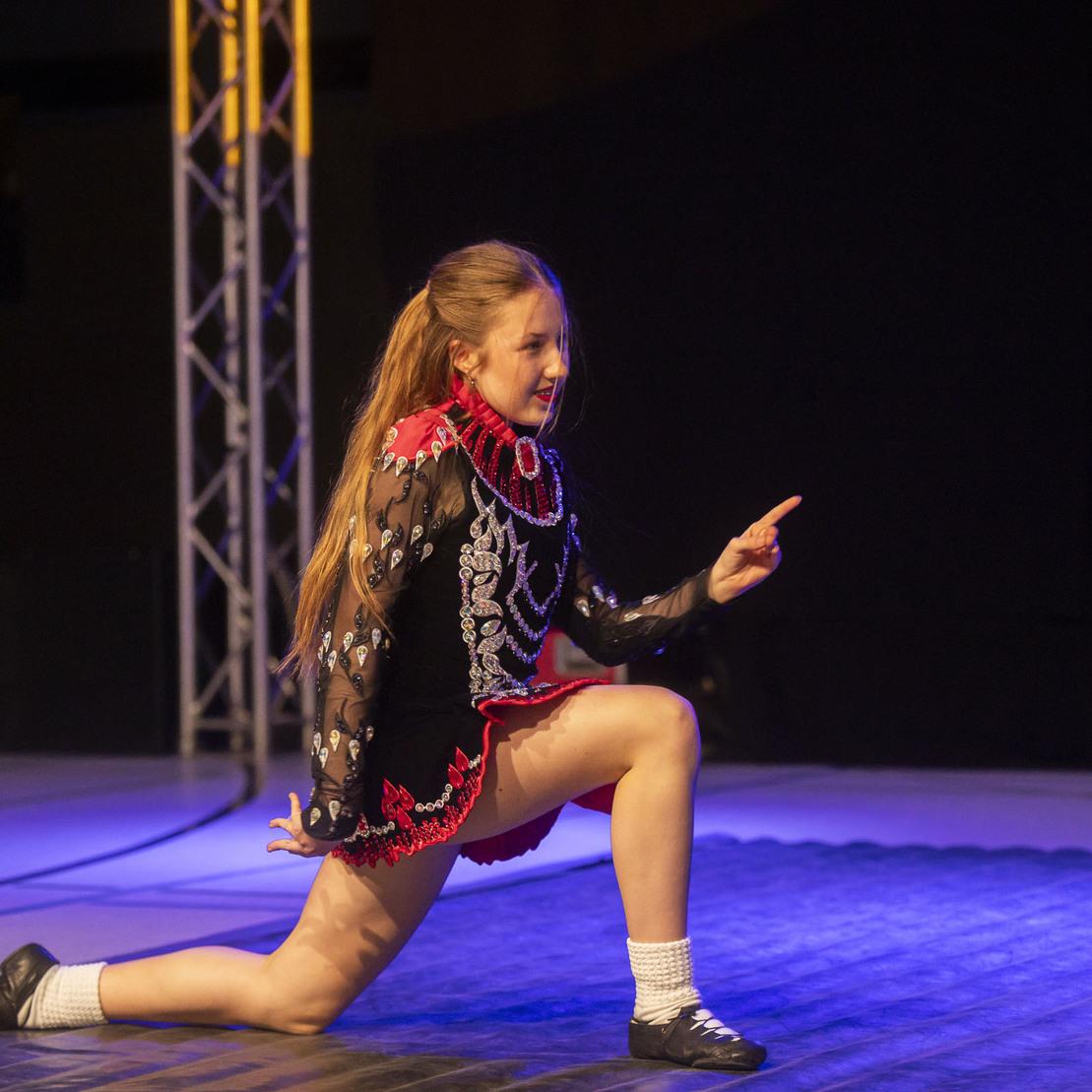 M&auml;dchen in traditioneller Tracht, die auf einem Wettkampf-Podest eine t&auml;nzerische Pose einnimmt.