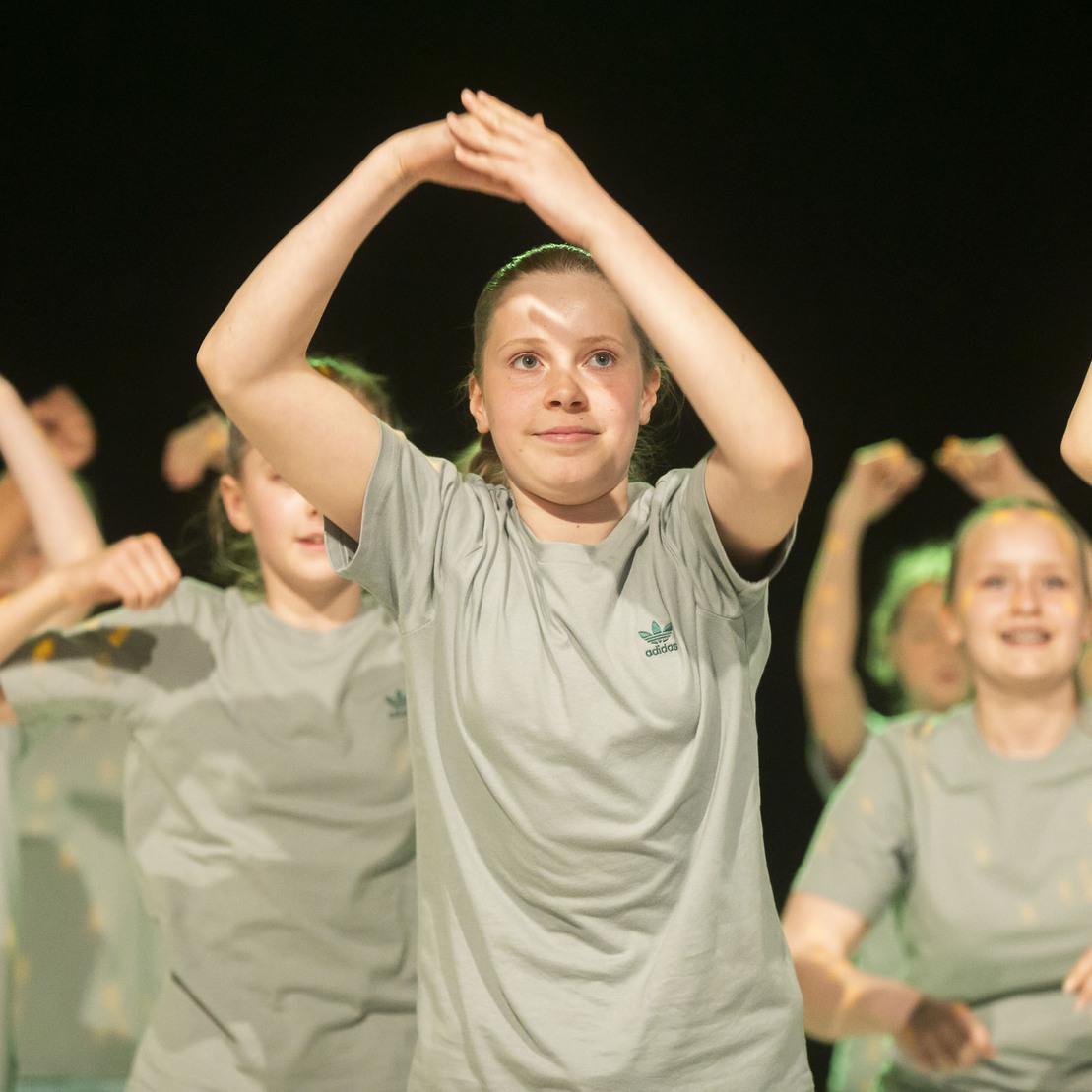 Gruppentanzauff&uuml;hrung mit Jugendlichen in grauen T-Shirts, die synchron Bewegungen ausf&uuml;hren und Freude ausstrahlen.