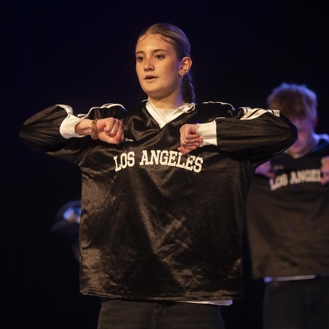 T&auml;nzerin in schwarzem Pullover mit Aufschrift &bdquo;LOS ANGELES&ldquo; beim Auftritt auf einer B&uuml;hne.
