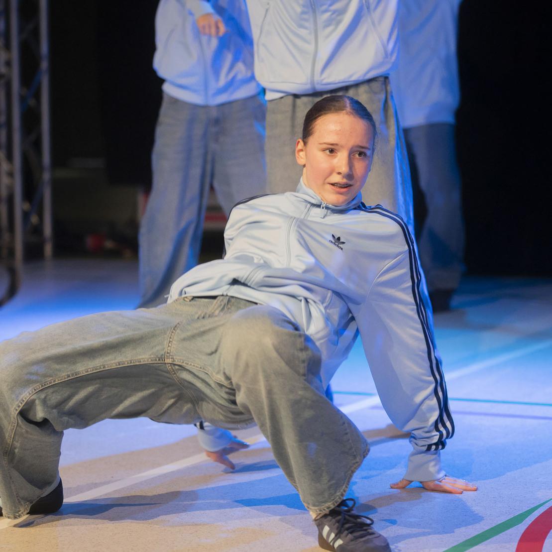 T&auml;nzerin in sportlicher Kleidung zeigt eine Pose auf einer B&uuml;hne w&auml;hrend einer Tanzauff&uuml;hrung.