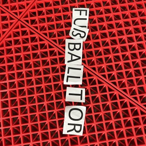 Buchstabenschnipsel mit dem Wort "Fu&szlig;balltor" auf einer roten, strukturierten Unterlage.