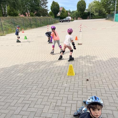 Kinder fahren auf Rollschuhen und umgehen kleine Pylonen auf einem gepflasterten Platz. Ein Kind sitzt im Vordergrund.