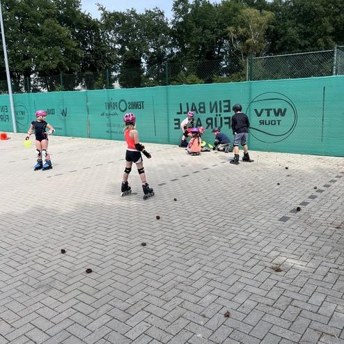 Kinder in Schutzausr&uuml;stung &uuml;ben auf einem Platz mit Drahtzaun, einige sind auf den Knien, andere stehen.