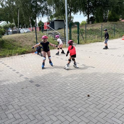 Kinder fahren auf einem gepflasterten Platz inline Skate, einige tragen Helme und Schutzausr&uuml;stung.