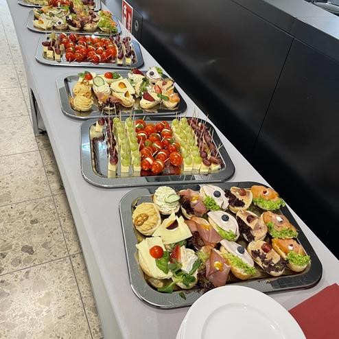 Buffet mit mehreren Platten, gefüllt mit Canapés, Trauben, Cocktailtomaten und anderen Vorspeisen auf einem Tisch.