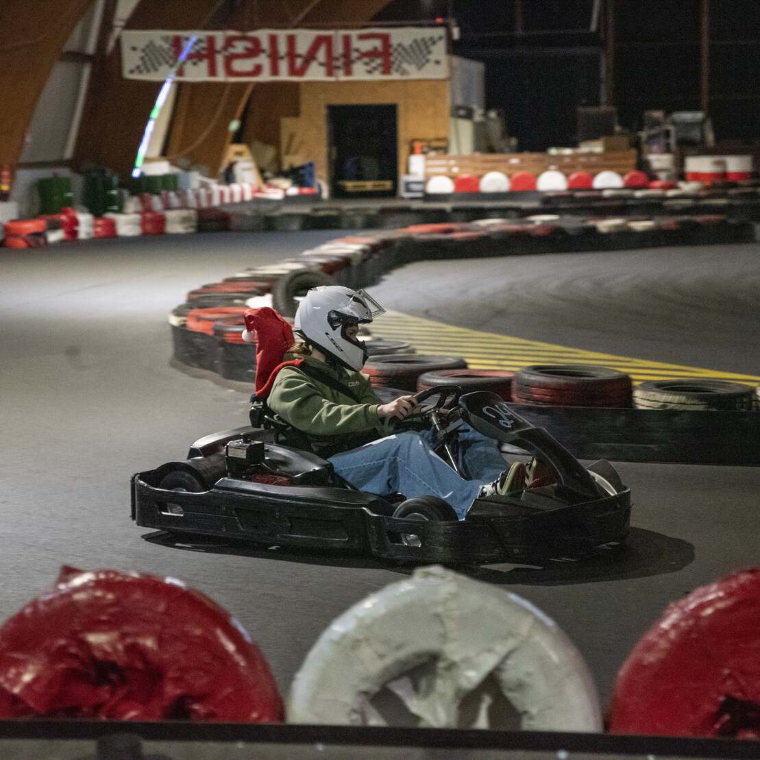 Kartfahrer auf Innenbahn bei Nacht, umgeben von Reifenstapeln und einer neongeschriebenen Zielanzeige.