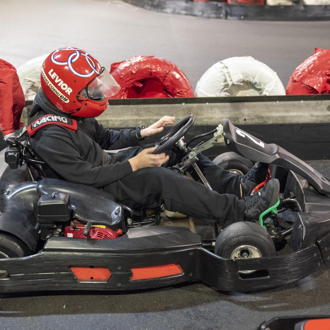 Junger Fahrer im Kartsport mit Helm steuert ein Go-Kart auf einer Rennstrecke mit roten und wei&szlig;en Reifen im Hintergrund.
