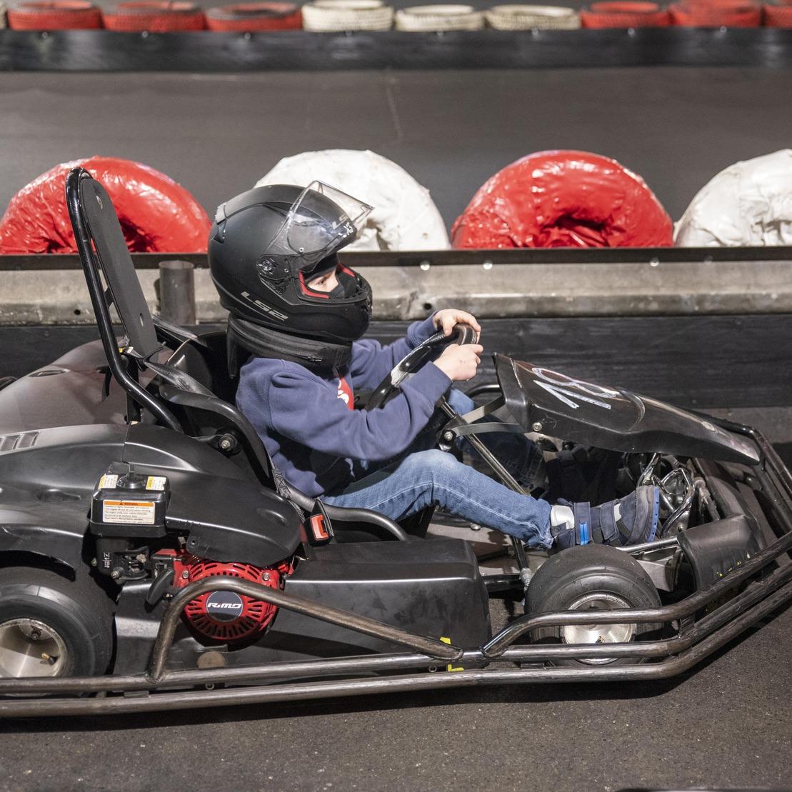 Junge f&auml;hrt in einem gokart auf einer Kartbahn, umgeben von Sicherheitsbarrieren in roten und wei&szlig;en Farben.