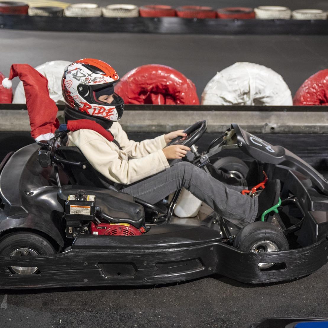 Kind in einem Kartsportanzug mit Helm f&auml;hrt in einem Go-Kart auf einer Rennstrecke mit roten und wei&szlig;en Pylonen.