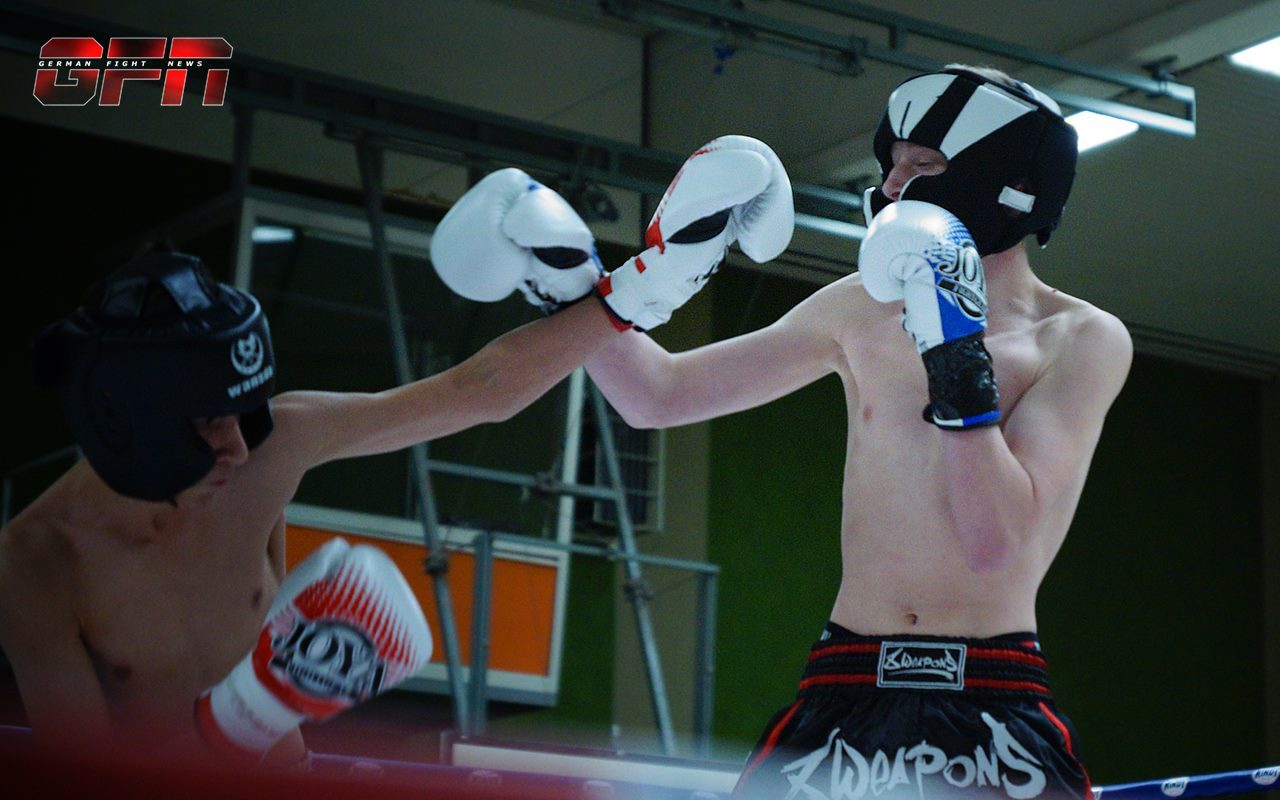 Zwei Boxer im Ring f&uuml;hren einen Schlagabtausch, beide tragen Schutzausr&uuml;stung und Boxhandschuhe.