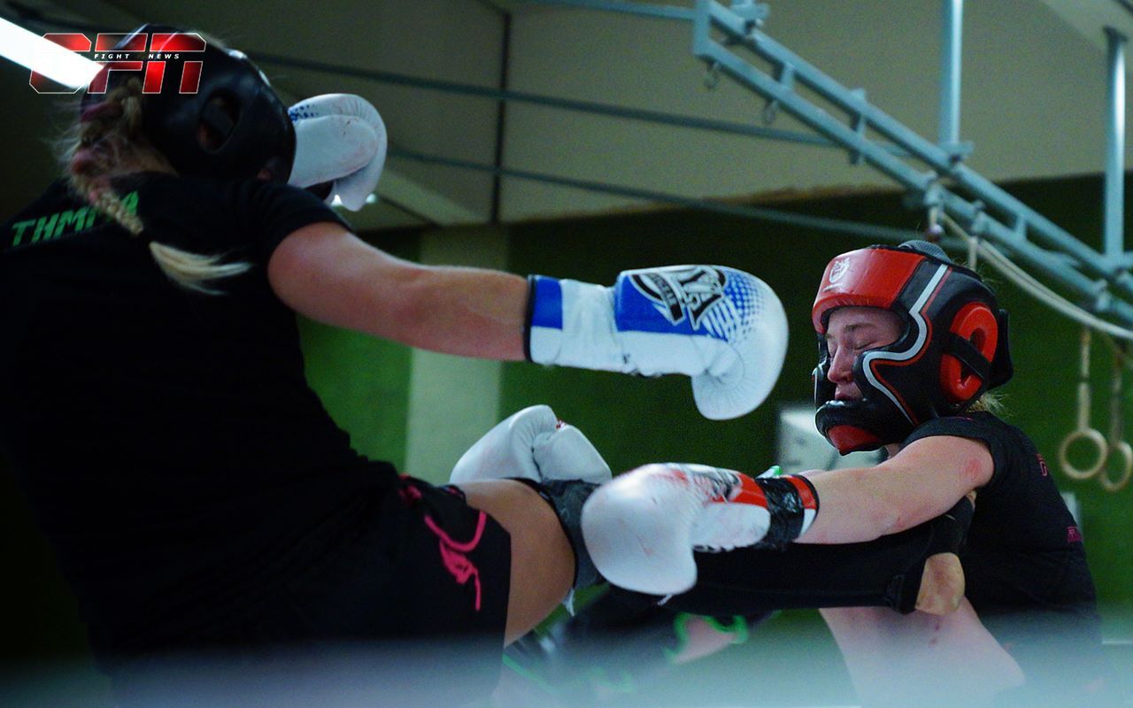 Zwei K&auml;mpferinnen im Sparring, eine tritt zu, die andere blockt mit Schutzausr&uuml;stung und Boxhandschuhen.