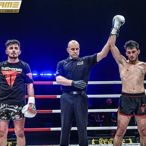 Zwei Kampfsportler stehen im Ring, w&auml;hrend der Schiedsrichter den Sieger verk&uuml;ndet. Dunkler Hintergrund mit Beleuchtung.