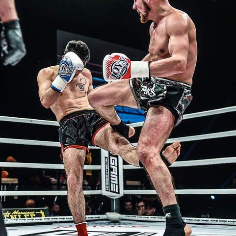 Zwei K&auml;mpfer in einem Ring, einer trifft den anderen mit einem Knie in einem intensiven Moment des Kickboxens.