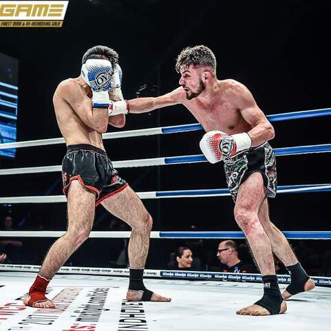 Zwei K&auml;mpfer in einem Ring, einer wirft einen Schlag, der andere weicht aus, umgeben von einer Zuschauermenge.