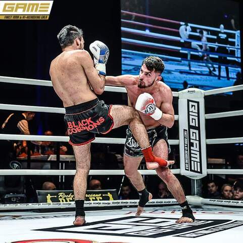 Zwei K&auml;mpfer im Ring bei einem Wettkampf, einer f&uuml;hrt einen Kick aus, w&auml;hrend der andere blockt.