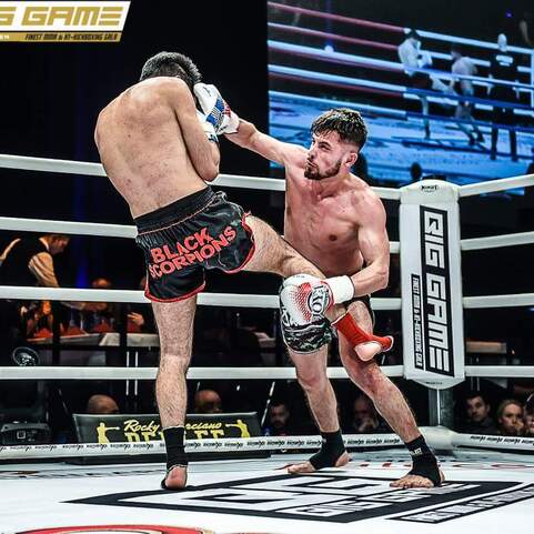 Zwei K&auml;mpfer stehen im Ring: Ein Mann f&uuml;hrt einen Kick gegen einen anderen, der sich defensiv abduckt.