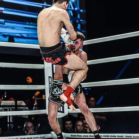 Zwei K&auml;mpfer im Ring; einer hebt den anderen an, w&auml;hrend das Publikum im Hintergrund zuschaut.