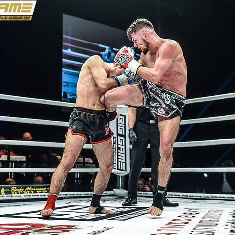 K&auml;mpfer in einem Ring, einer f&uuml;hrt einen Knieangriff gegen seinen Gegner aus, w&auml;hrend Publikum zuschaut.