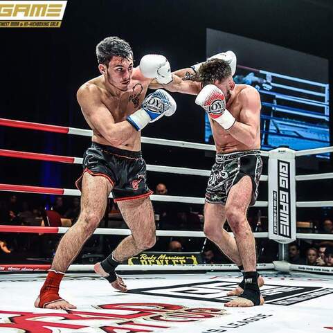 Zwei K&auml;mpfer im Ring w&auml;hrend eines Wettkampfs im Muay Thai, einer setzt einen Schlag gegen den anderen ab.