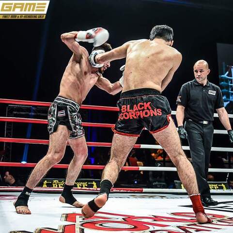 Zwei K&auml;mpfer im Ring, einer schl&auml;gt mit Handschuhen zu, w&auml;hrend der Schiedsrichter aufmerksam beobachtet.