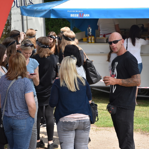 Gruppe von Menschen, die an einem Verkaufsstand stehen, einige essen und Getr&auml;nke in der Hand halten.