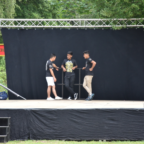 Drei junge M&auml;nner stehen auf einer B&uuml;hne mit schwarzem Hintergrund und diskutieren miteinander.