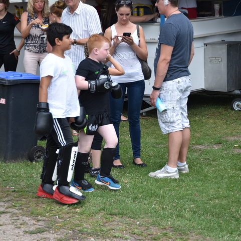 Zwei Kinder in Boxausr&uuml;stung gehen an einer Menschenmenge vorbei, w&auml;hrend Erwachsene miteinander sprechen.